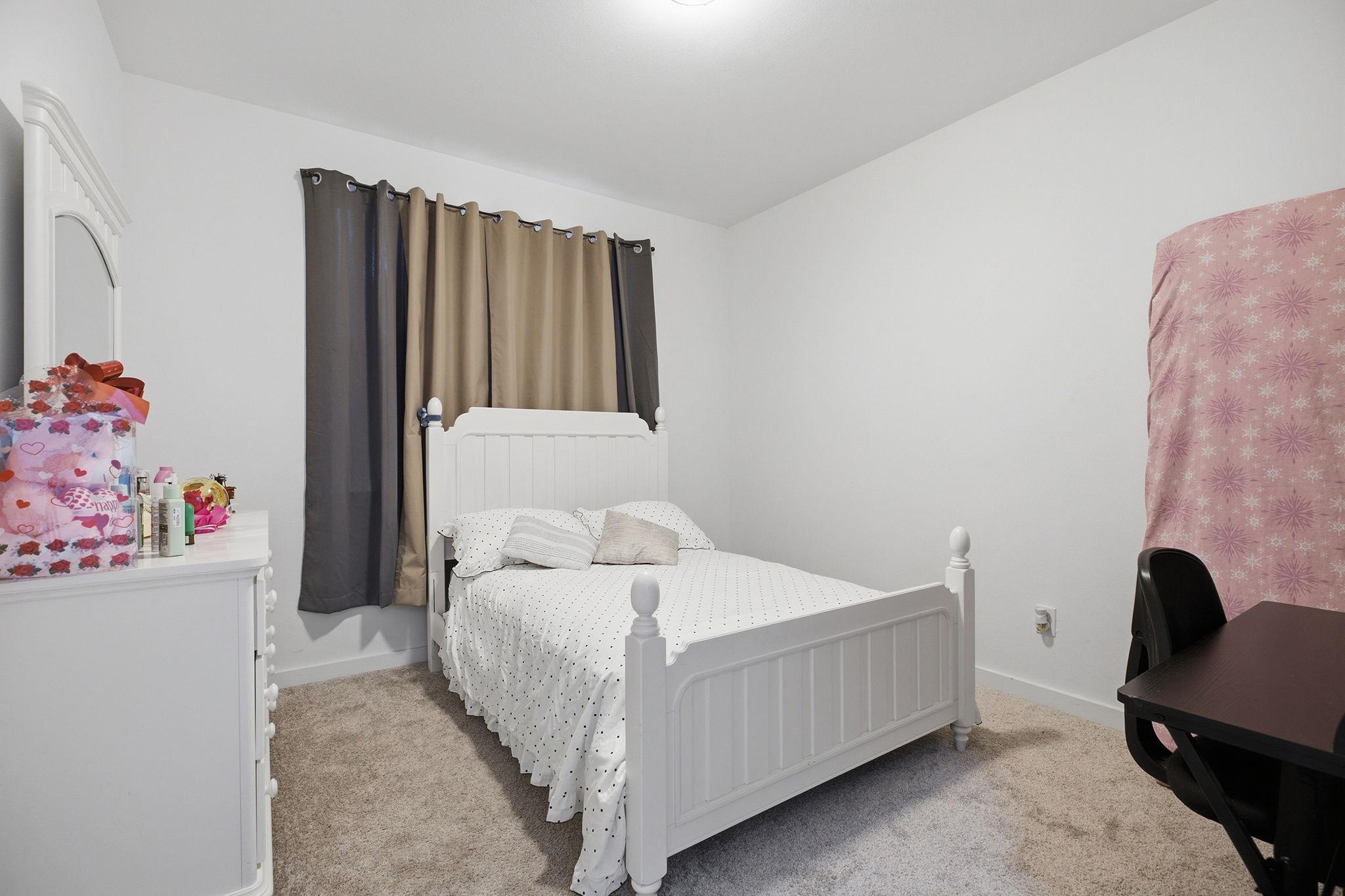 Bedroom with a white bed, dotted bedding, gray and tan curtains, and beige carpet.