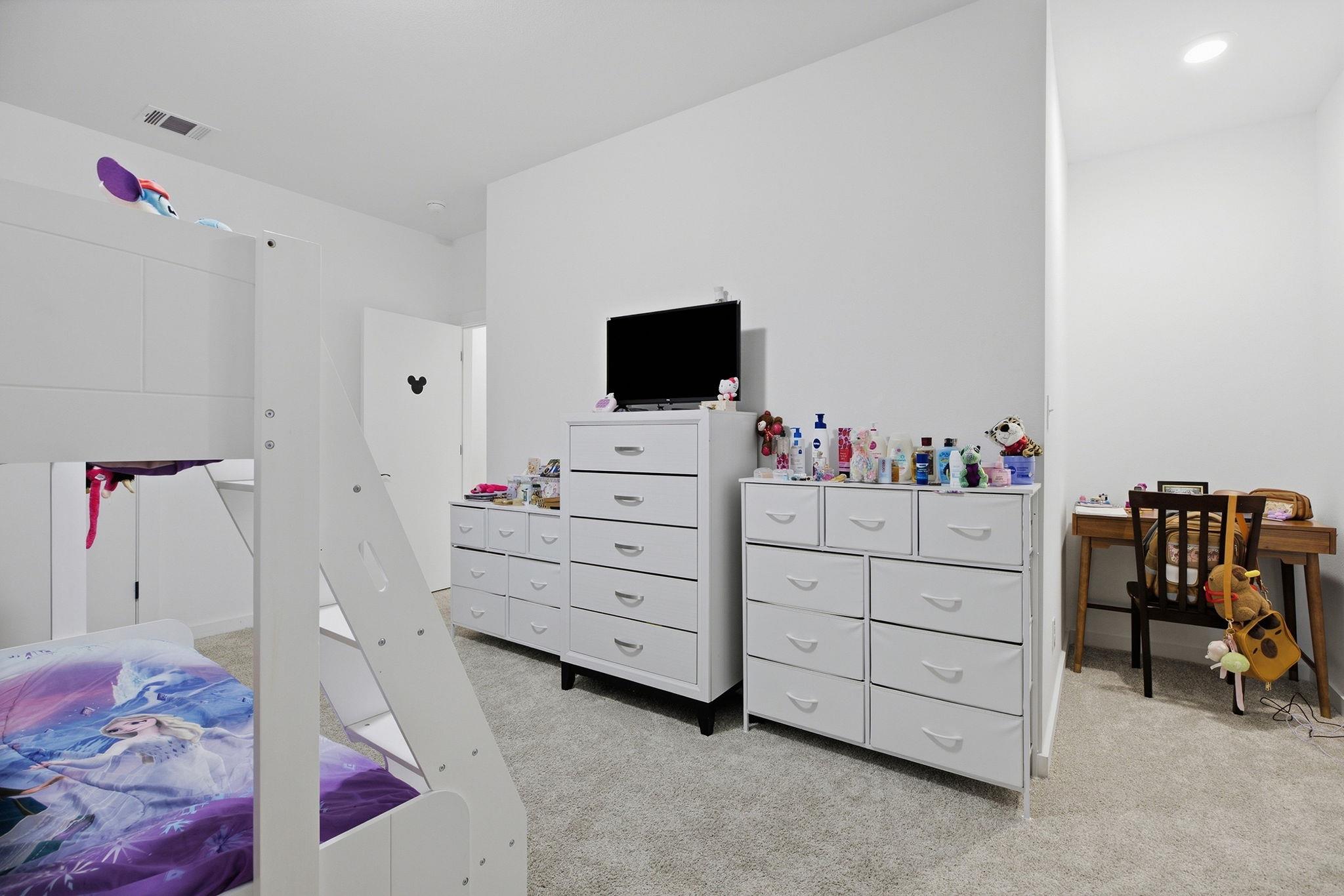 Children’s bedroom with a white loft bed, purple bedding, white dressers, and a small desk.