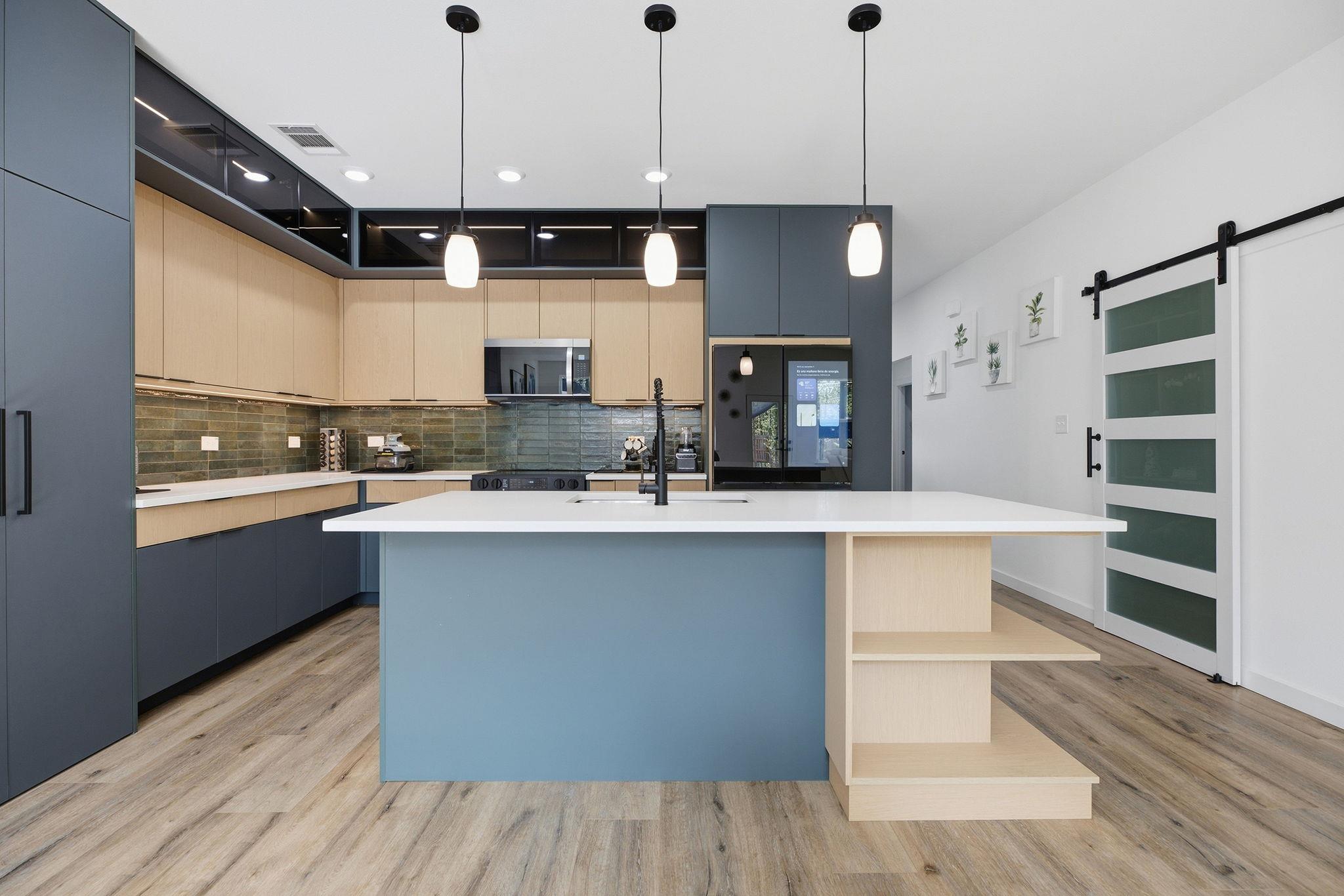 Modern kitchen with a blue island, light wood cabinetry, and dark green tile backsplash.
