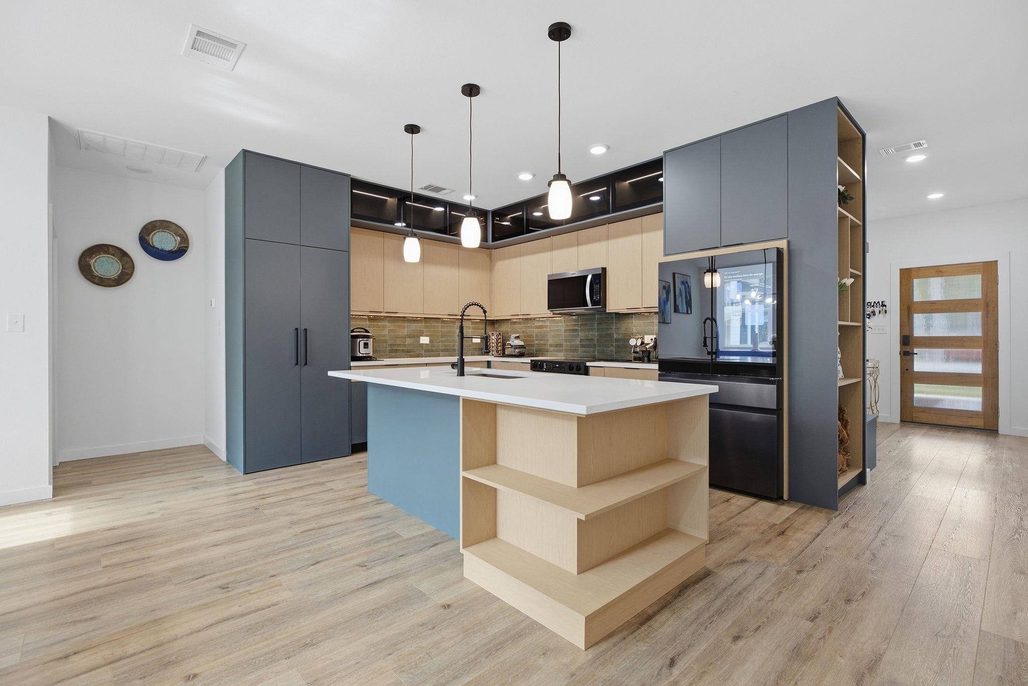 Modern kitchen with a large wood island, slate-blue cabinets, and pendant lights.