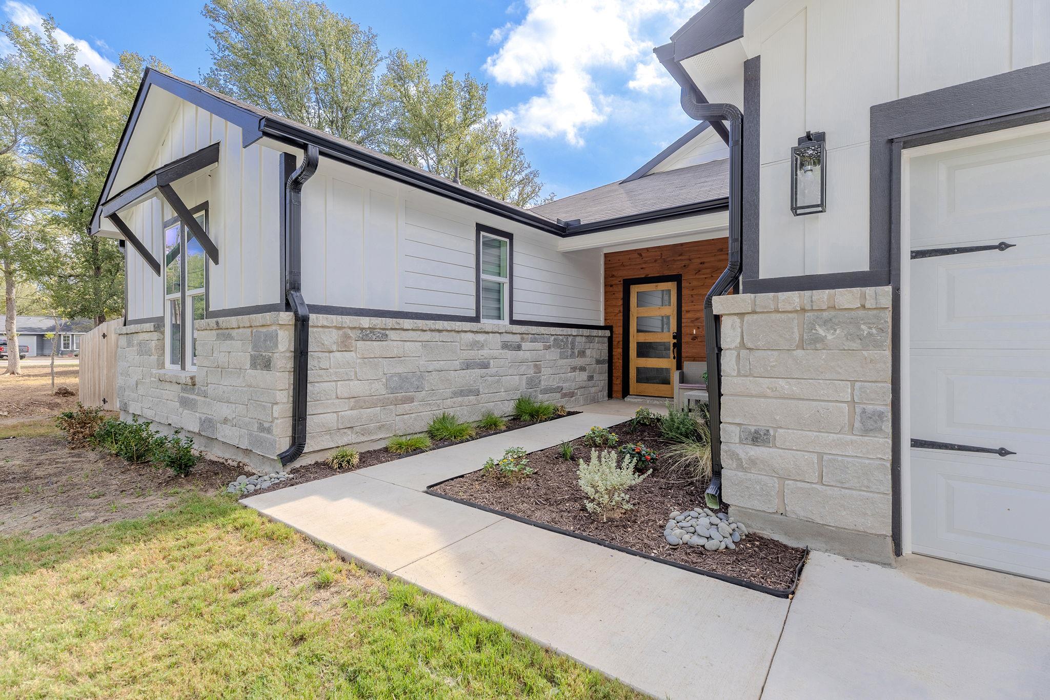 Modern white house with stone facade, landscaped walkway, and recessed wood entry door.