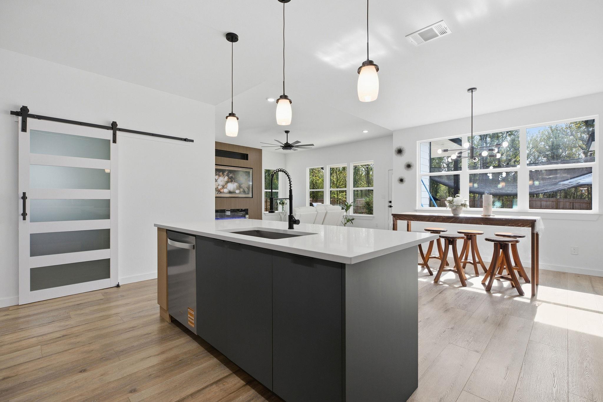 Modern kitchen with a large island, dark cabinets, pendant lights, and a frosted-panel barn door.