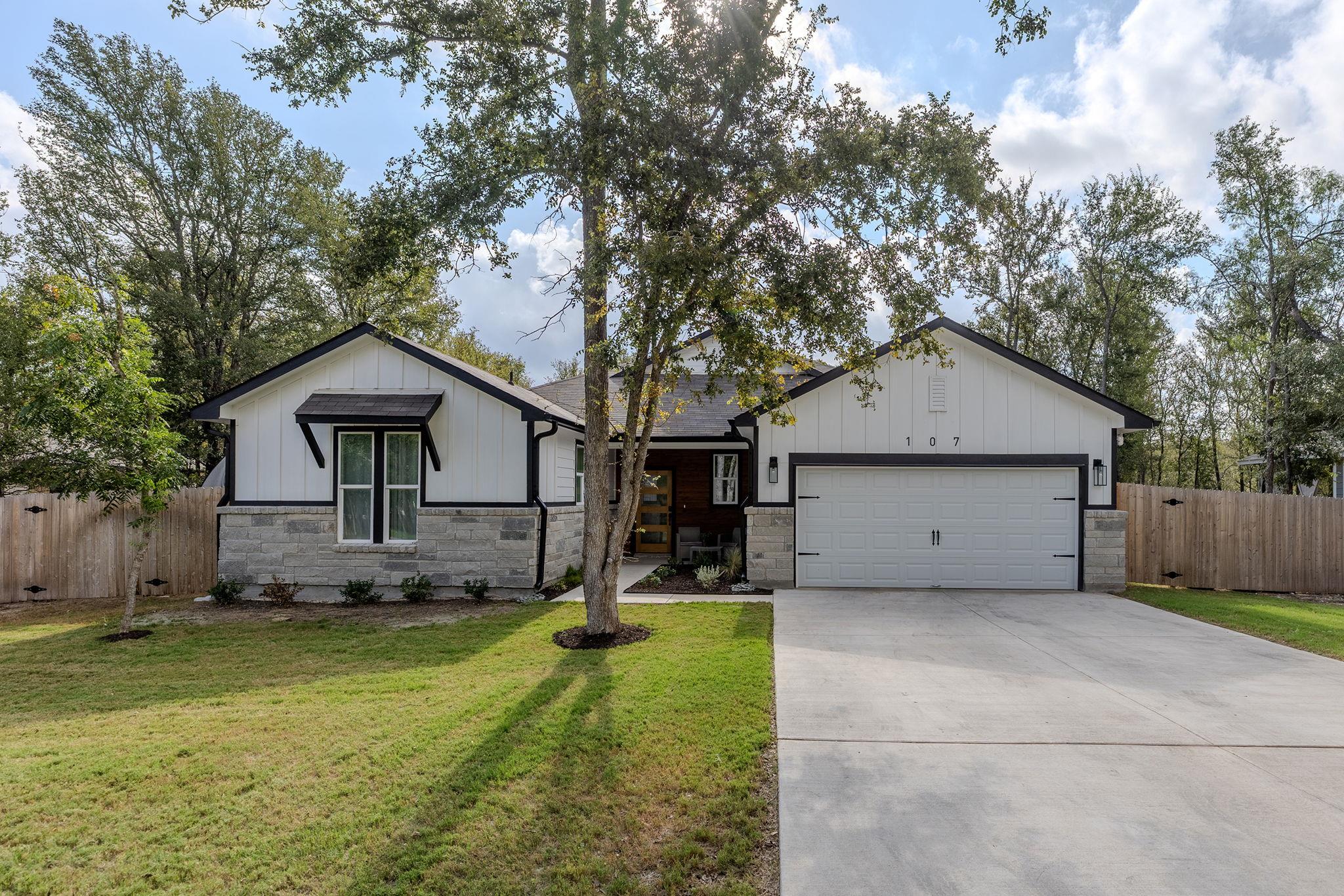 White single-story home with stone accents, dark trim, and a mature tree in the front lawn.