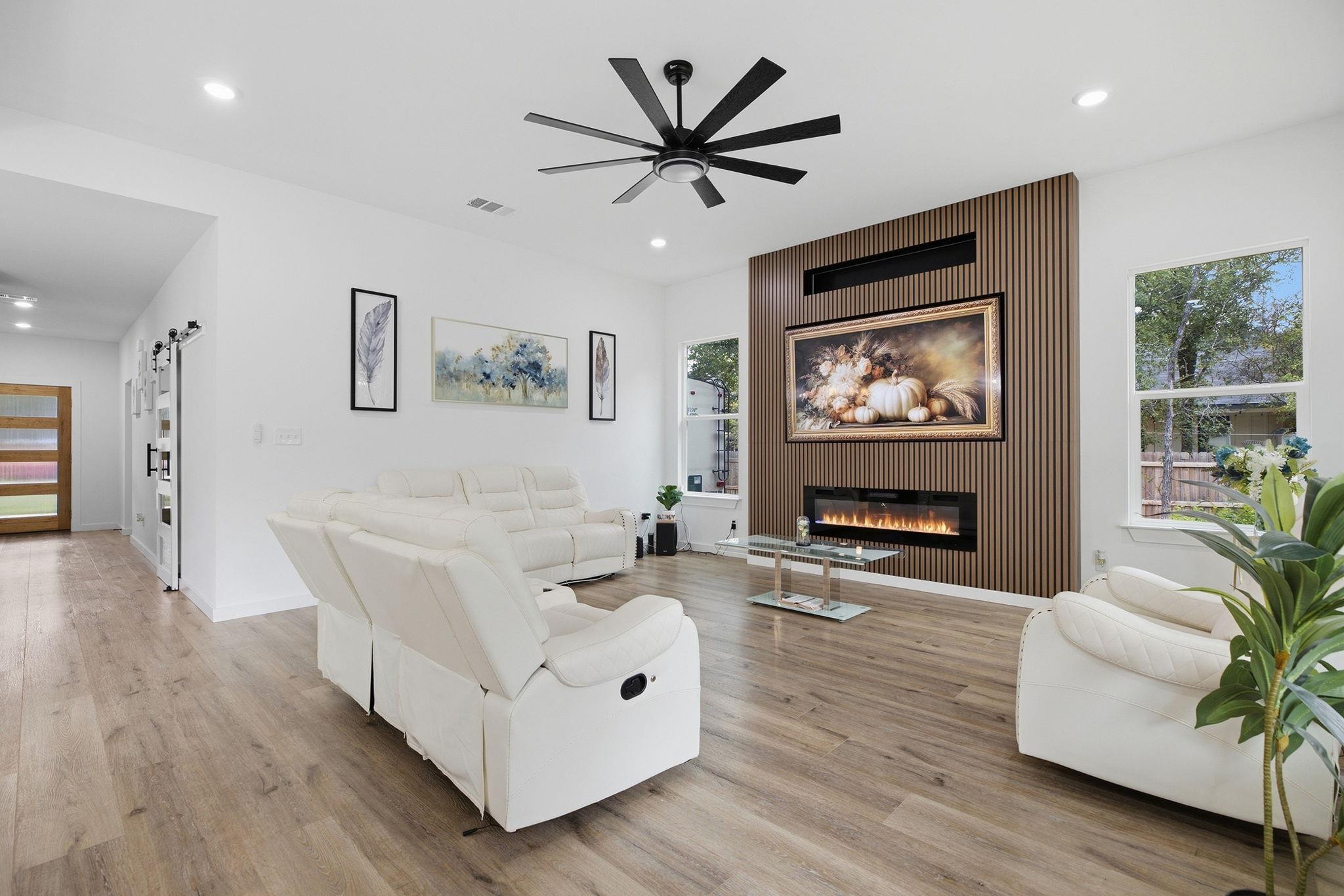 Living room with white reclining sofas, wood-slat fireplace wall, and light wood flooring.