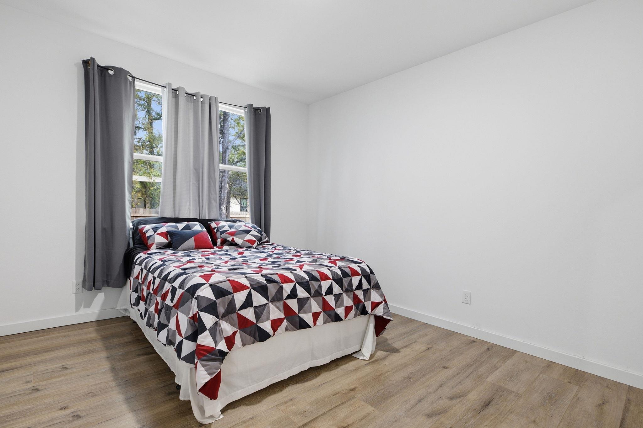 Bedroom with geometric-patterned bedding, gray curtains, and wood-look flooring.