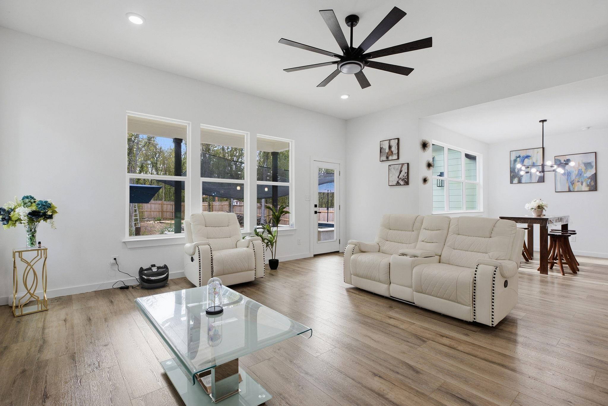 Furnished living room with cream reclining sofas, a glass coffee table, and large windows overlooking the patio.