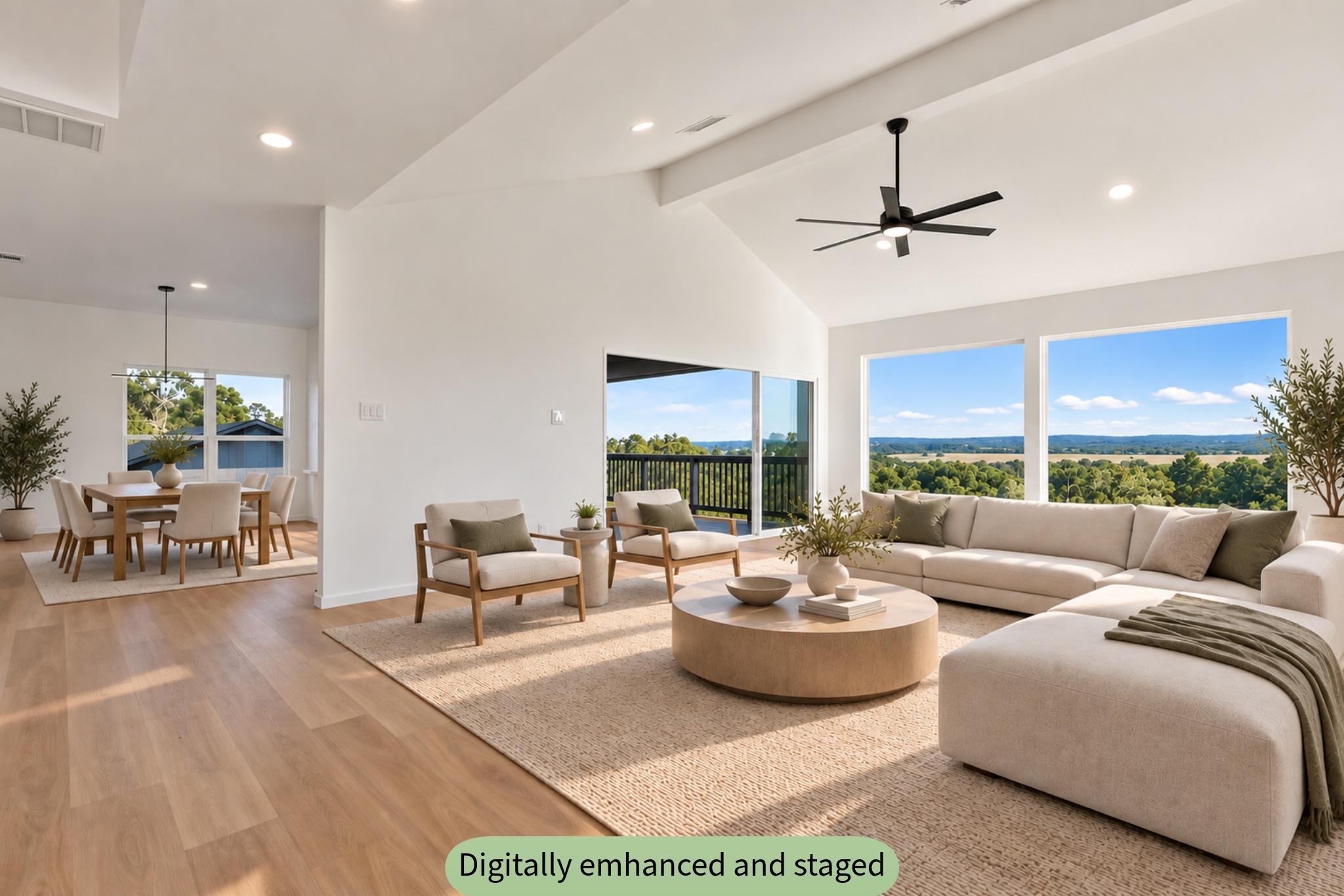 Staged open-plan living and dining room with a vaulted ceiling and large windows overlooking countryside.