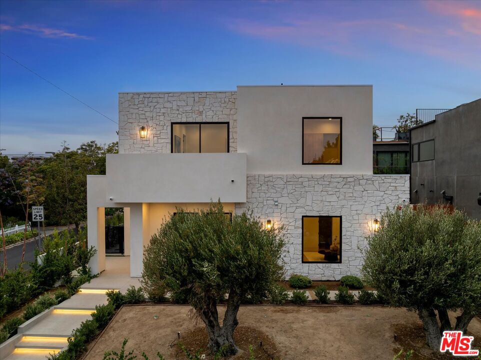 Modern stone-and-stucco home with black-framed windows and illuminated entry steps at dusk.