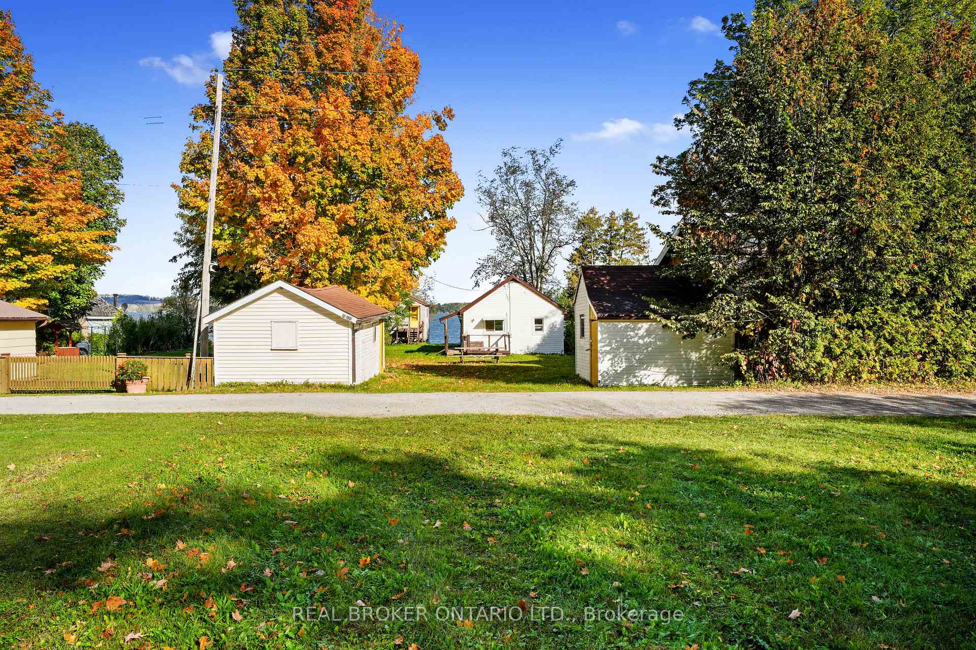 Small white buildings among autumn trees beside a grassy lane, with water visible in the distance.