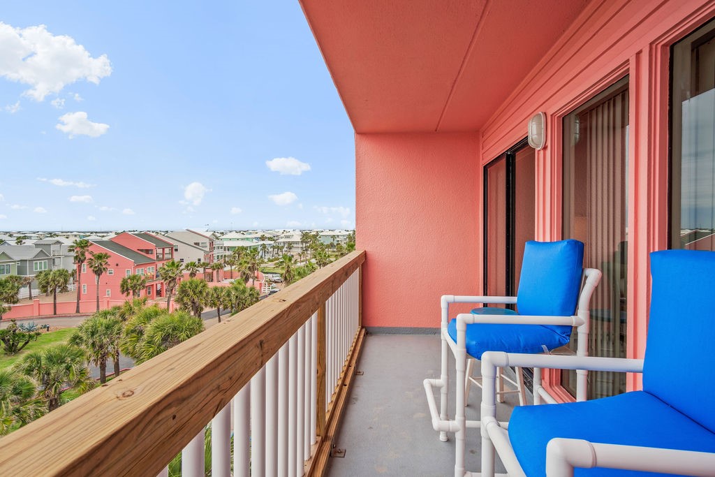 Covered balcony with blue chairs overlooking palm trees and coastal condominium buildings.