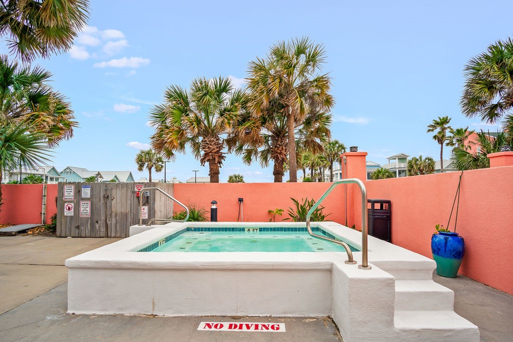 Outdoor pool with white steps, turquoise water, coral walls, and palm trees.