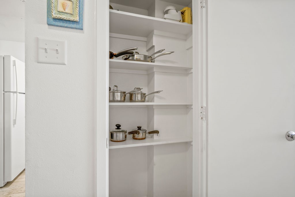 Open kitchen pantry with pots and pans arranged on white shelves.