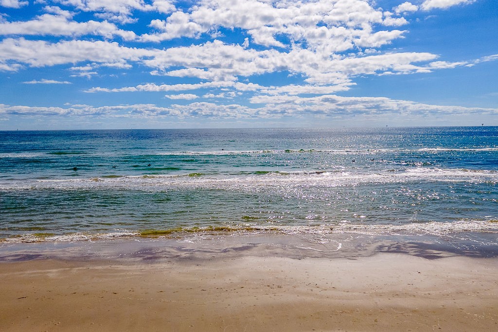 Sandy beach and gentle Gulf waves beneath a blue, cloud-filled sky.