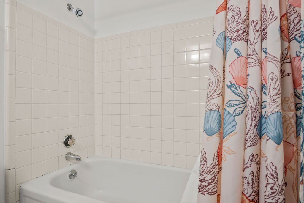White tiled bathtub and shower with a colorful seashell-patterned curtain.
