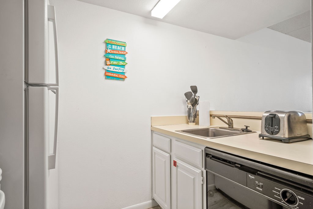 Compact kitchen with white cabinets, stainless appliances, and a colorful beach-themed wall sign.