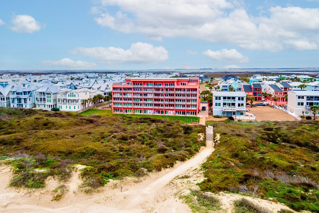 Aerial view of a red multistory condominium behind sandy paths and coastal scrub.