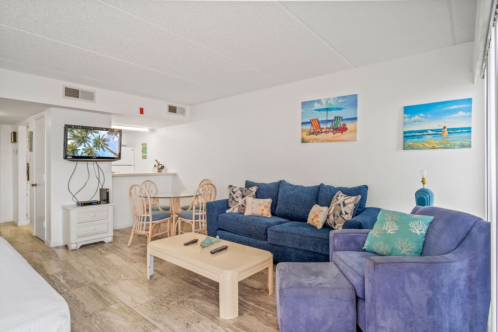 Furnished living room with a blue sofa, purple armchair, and beach-themed wall art.