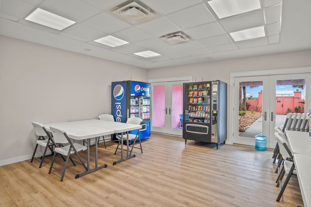 Communal break room with tables, folding chairs, drink and snack vending machines, and glass doors.