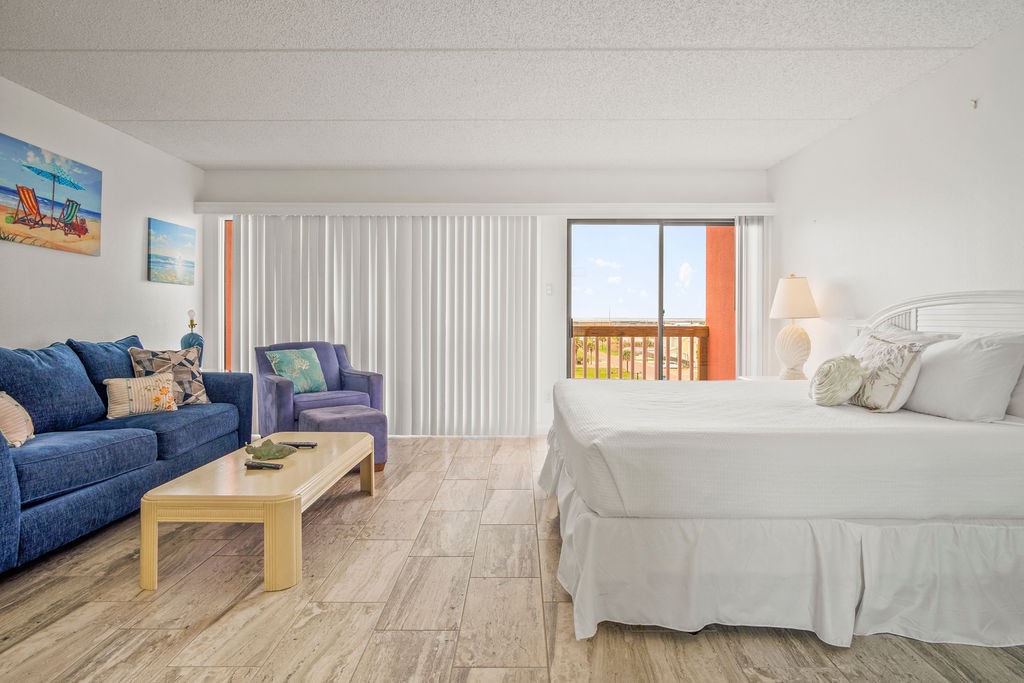Bedroom with a white bed, blue sitting area, and sliding glass door to a balcony.
