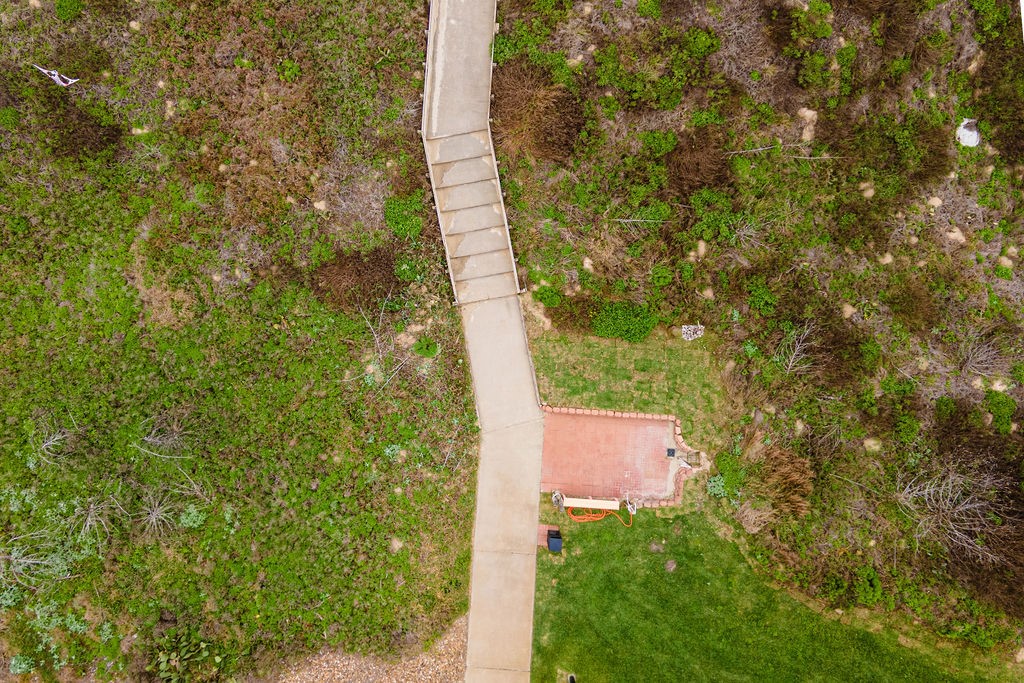 Aerial view of a walkway through coastal scrub leading to a brick patio and lawn.