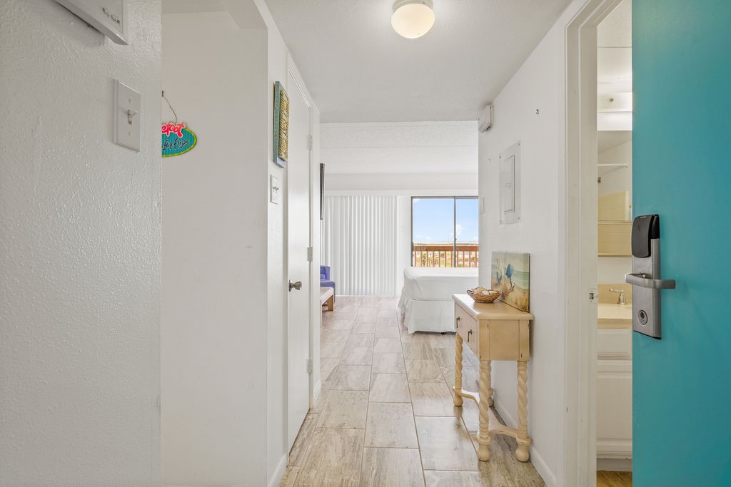 Condo hallway leading to a bedroom with a balcony window and a bathroom doorway.