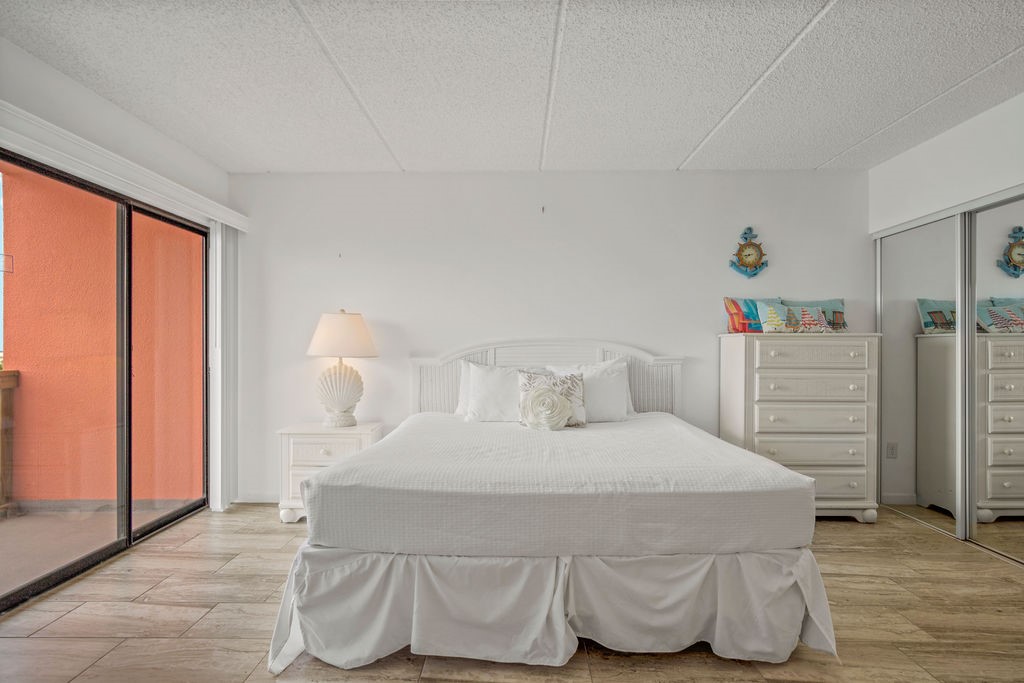 Furnished bedroom with a white bed, mirrored closet doors, and sliding glass doors to a patio.