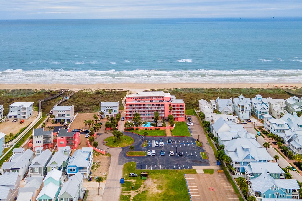 Beachfront condominium complex beside the ocean, with a pool, parking lot, and beach houses nearby.