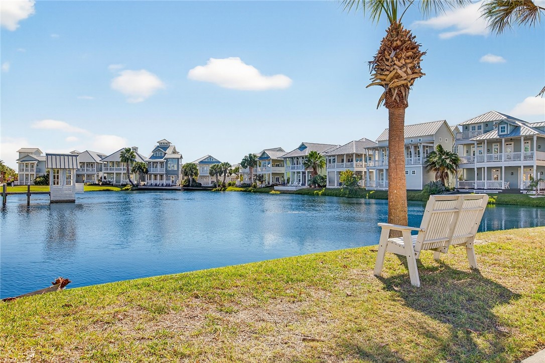 Lagoon waterfront with coastal-style homes across the water and chairs beneath a palm tree.