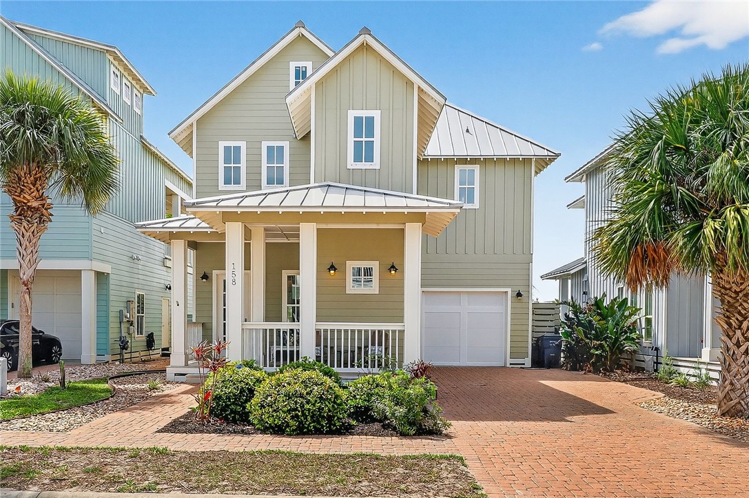 Two-story sage-green house with a covered porch, attached garage, and brick driveway.