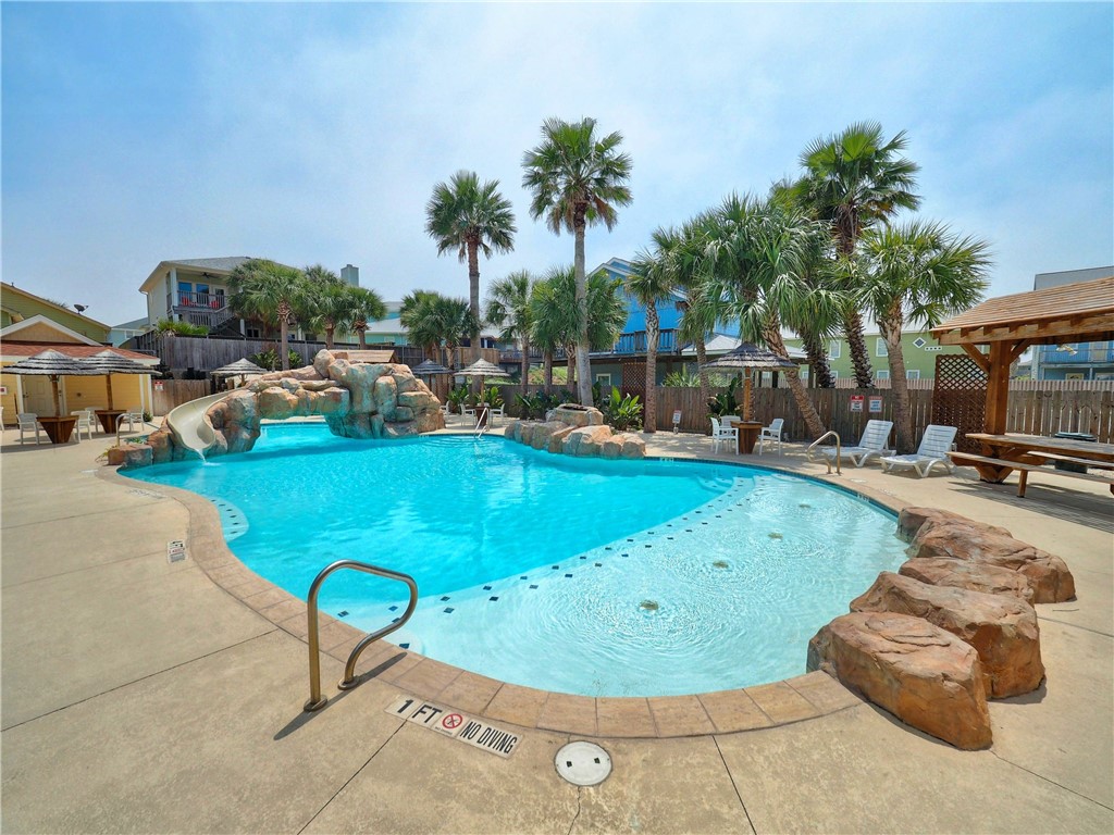 Outdoor pool with a rock waterfall, palm trees, and a shallow wading area.