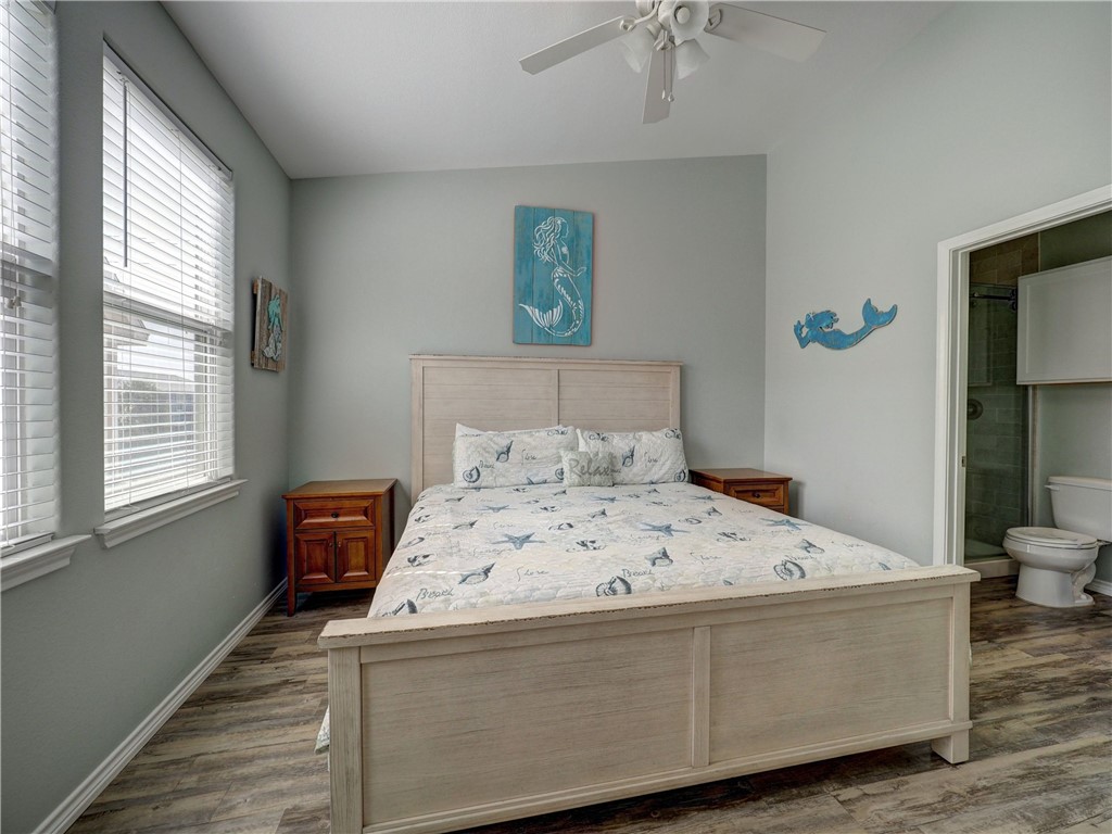 Bedroom with nautical bedding, a light-wood bed, large windows, and an adjoining bathroom.