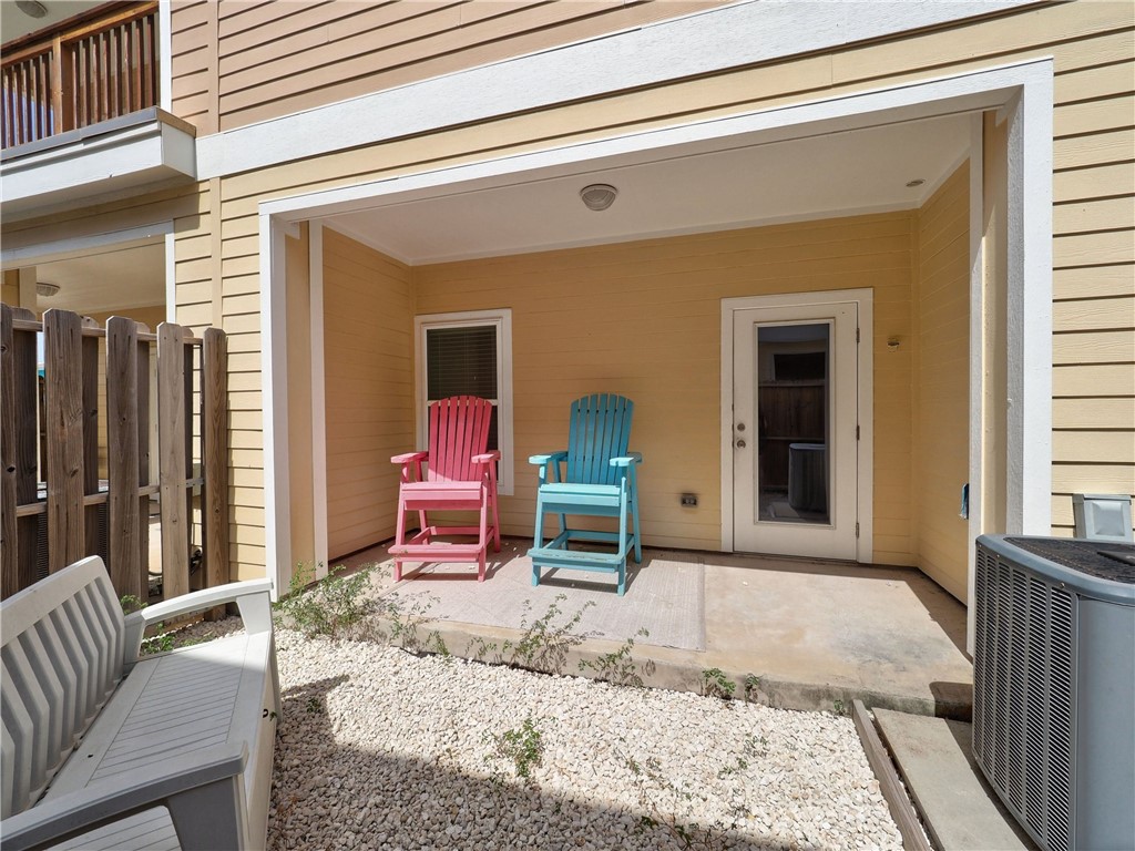 Covered patio with pink and turquoise Adirondack chairs beside a yellow-sided home.