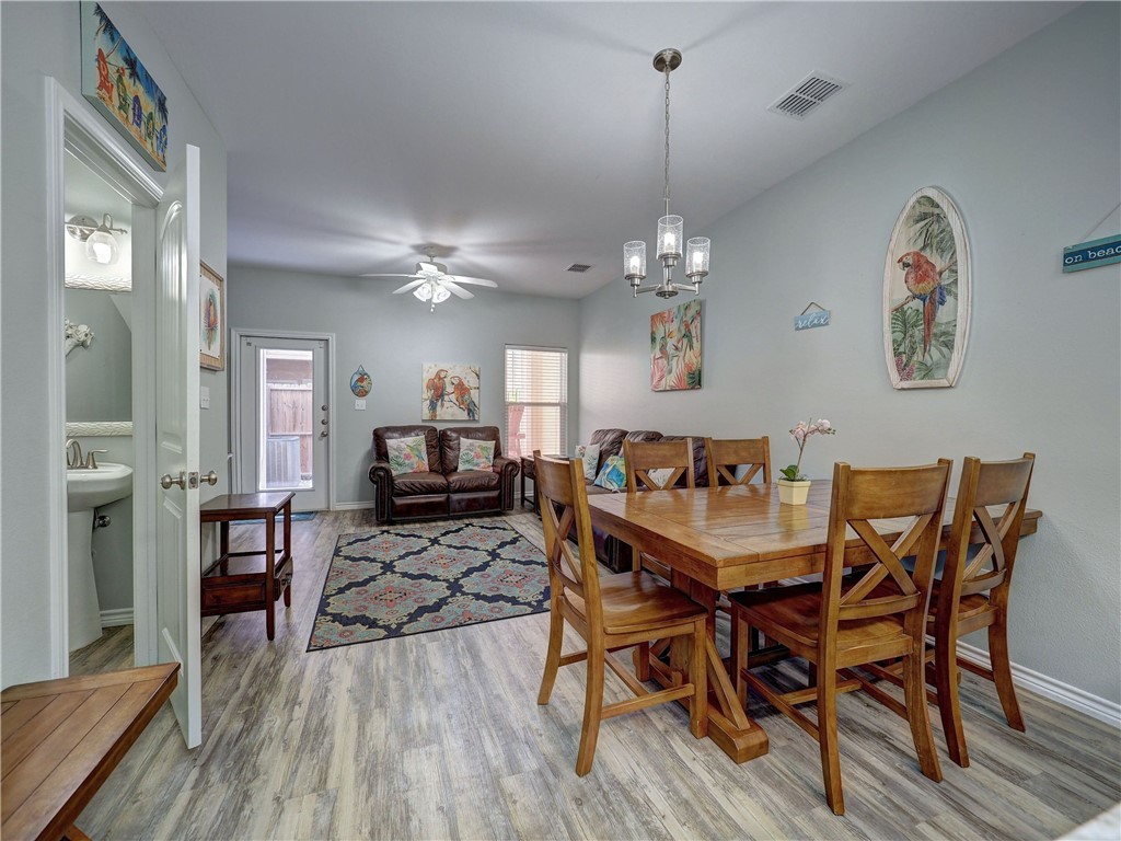 Dining and living area with a wooden table, leather loveseat, patterned rug, and tropical artwork.