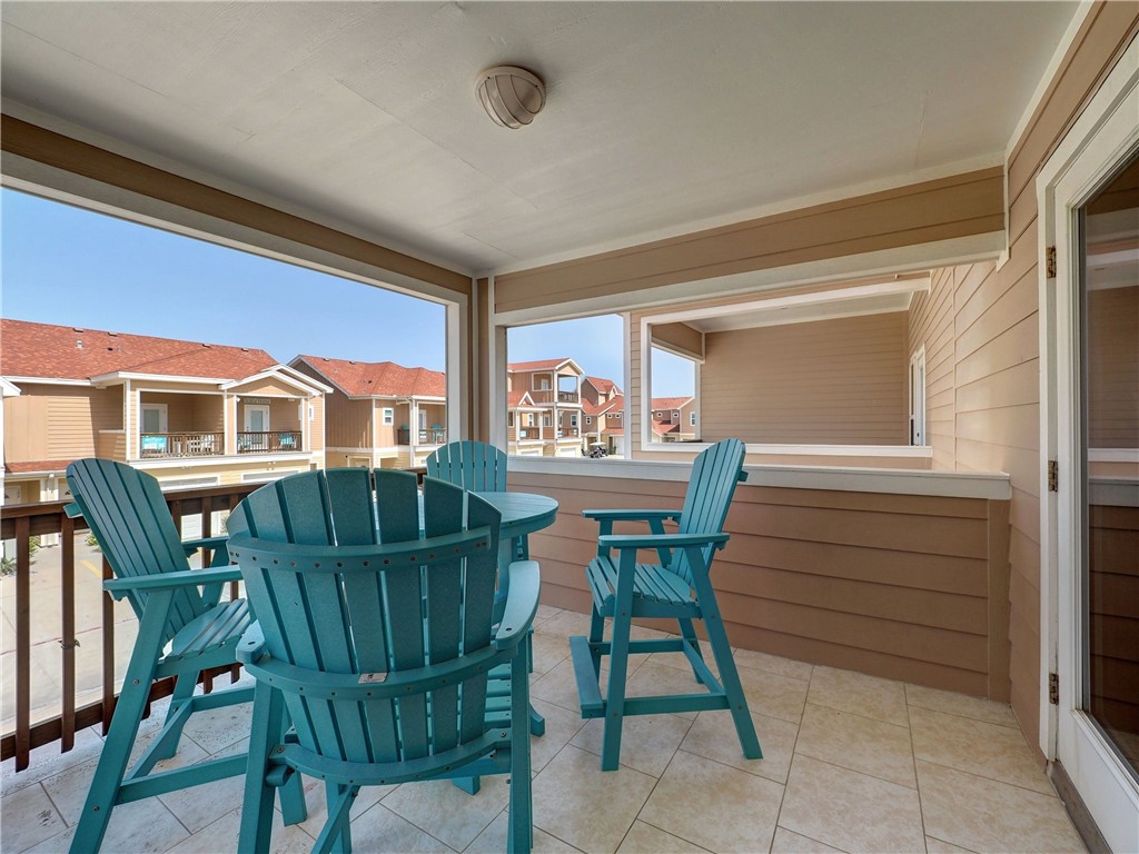 Covered balcony with teal Adirondack chairs and views of neighboring buildings.