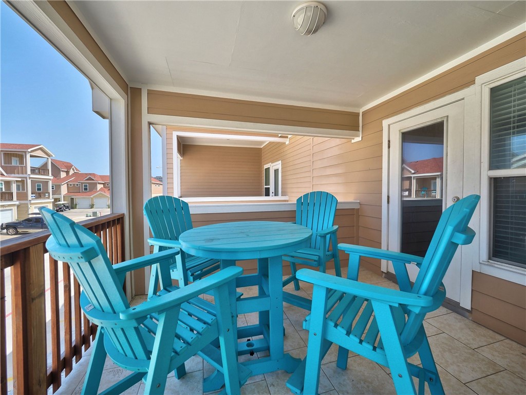 Covered balcony with turquoise Adirondack chairs around a round table, overlooking nearby homes.