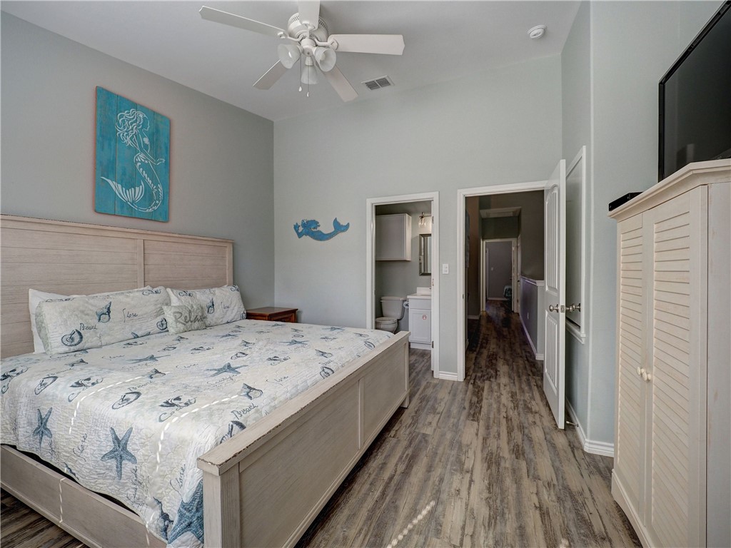 Furnished coastal-style bedroom with a light-wood bed, blue ocean-themed art, and bathroom doorway.