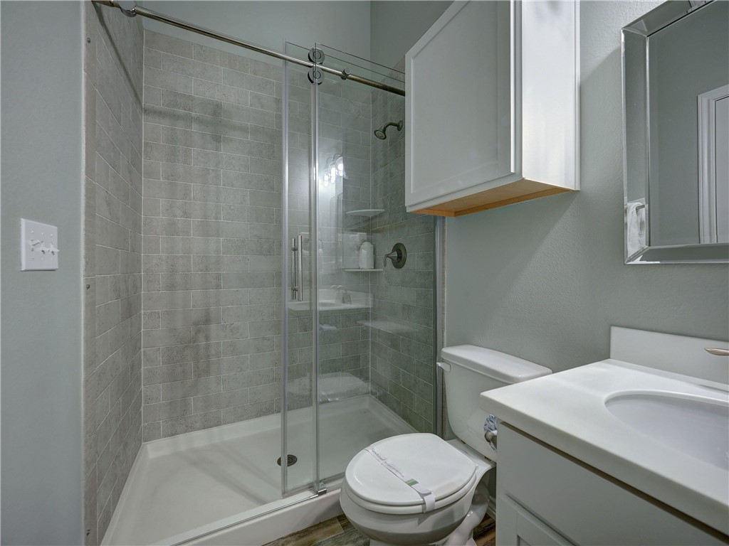 Bathroom with a gray-tiled glass shower, white vanity, and toilet.