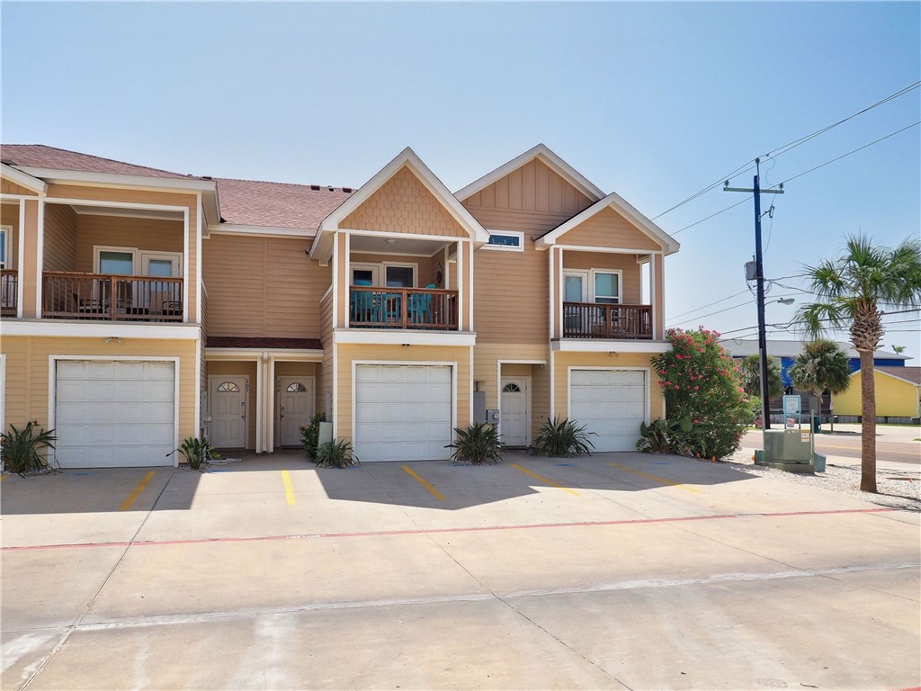 Tan two-story townhomes with balconies, garage doors, and parking spaces along the street.