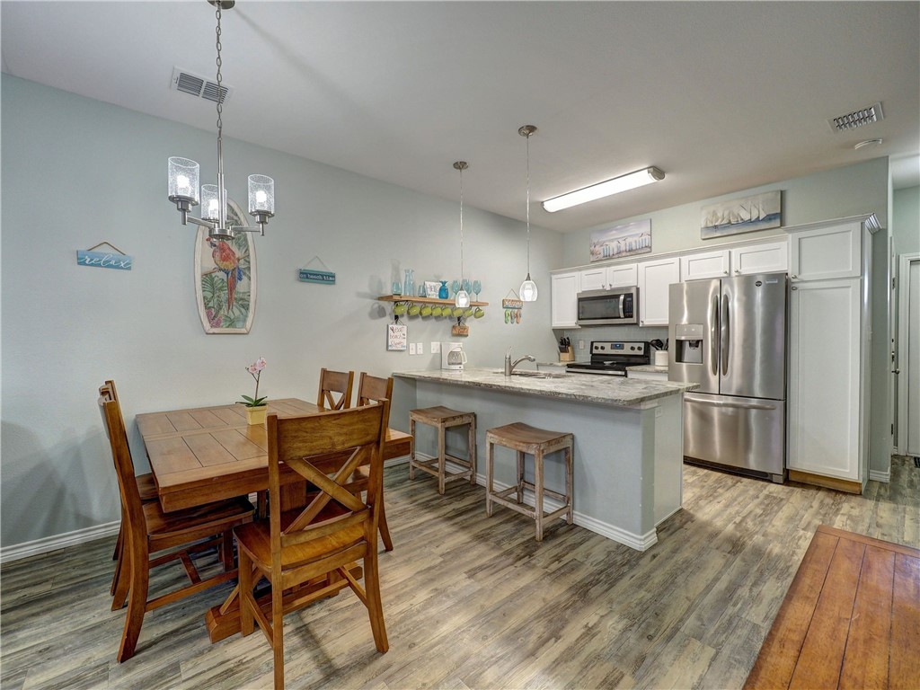 Kitchen and dining area with a wood table, white cabinets, stainless steel appliances, and island seating.