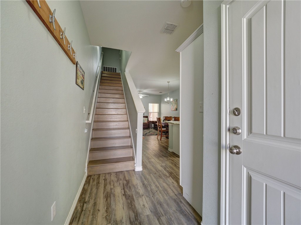 Entryway with a staircase, wood-look floors, and a view into the furnished living and dining area.