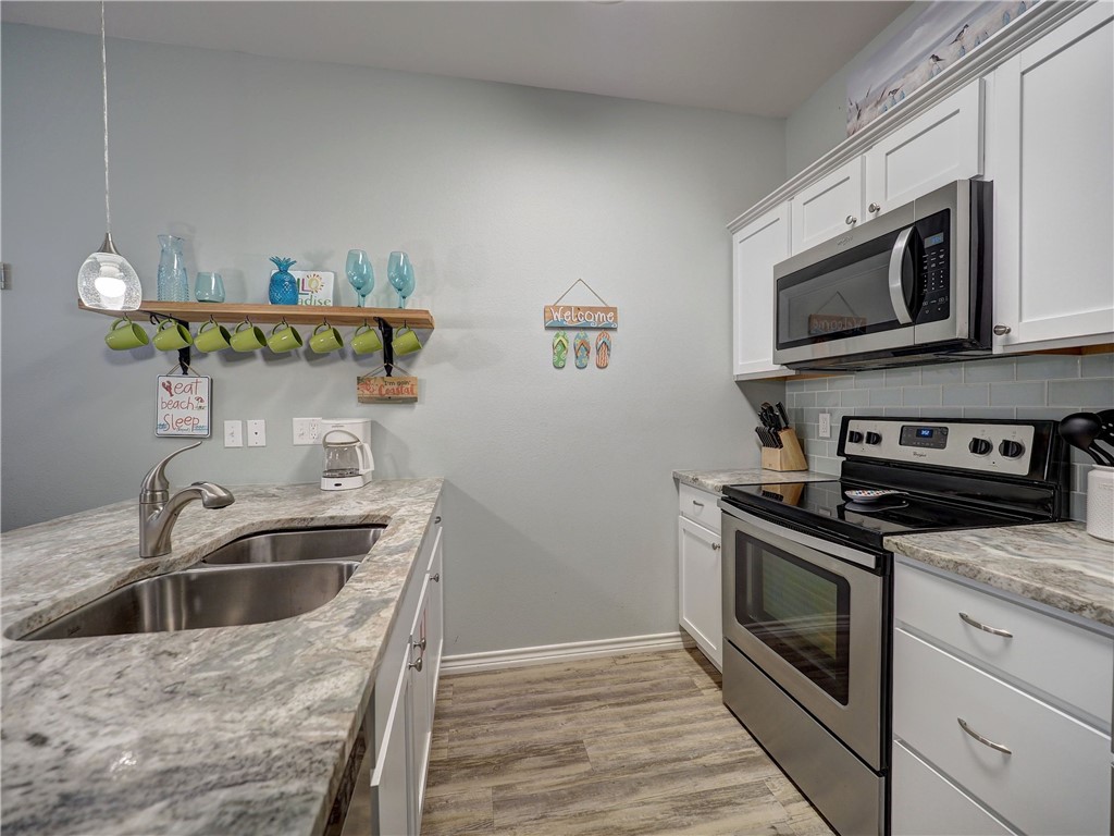 Kitchen with white cabinets, stone countertops, stainless-steel appliances, and green mugs hanging beneath a shelf.