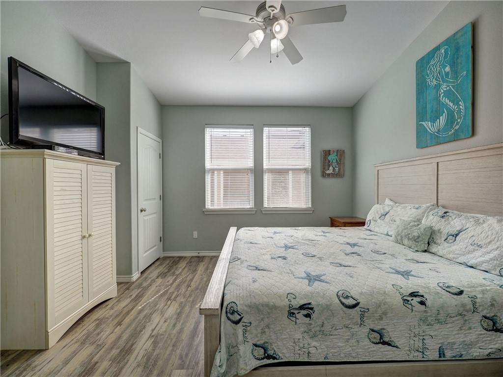 Bedroom with sea-life patterned bedding, two windows, a ceiling fan, and wood-look flooring.