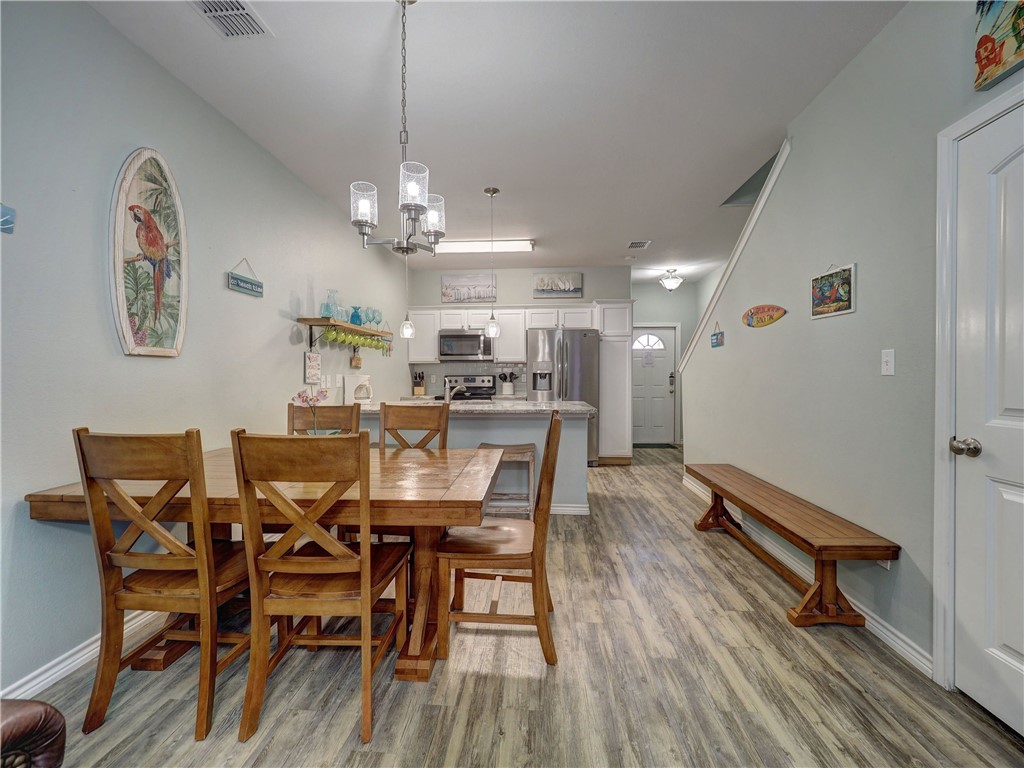 Dining area with a wooden table and chairs beside an open kitchen with stainless steel appliances.