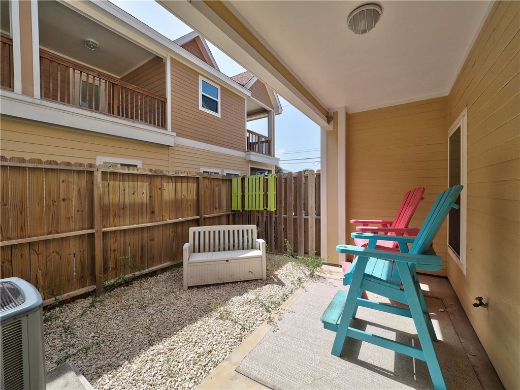 Covered patio with colorful Adirondack chairs, a white bench, and a gravel garden behind a wooden fence.