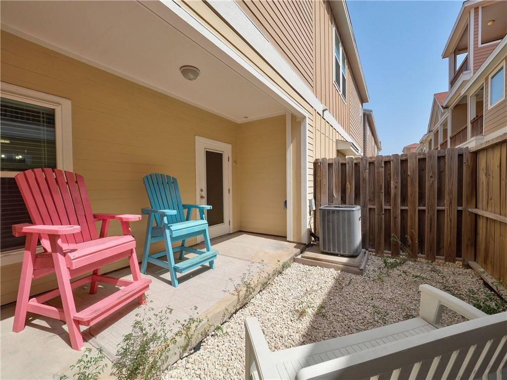 Condominium patio with pink and turquoise chairs beside a fenced gravel yard.