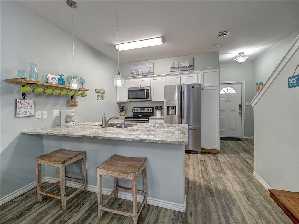 Condo kitchen with white cabinets, stainless steel appliances, and a breakfast bar with two wooden stools.