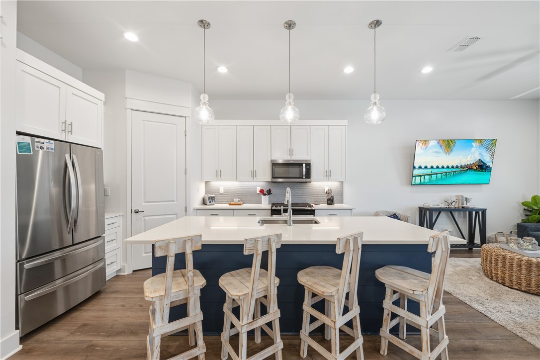 Kitchen with a navy island, white countertop, rustic bar stools, and stainless steel appliances.