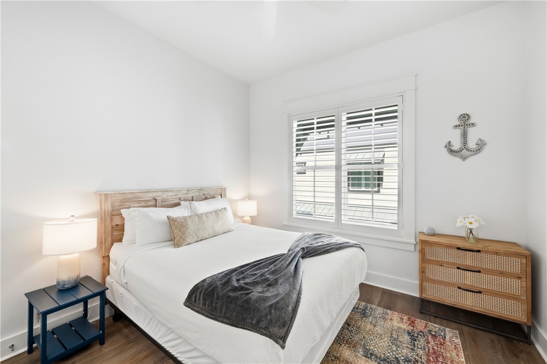 Bedroom with a white bed, shuttered window, and woven-front wood dresser.