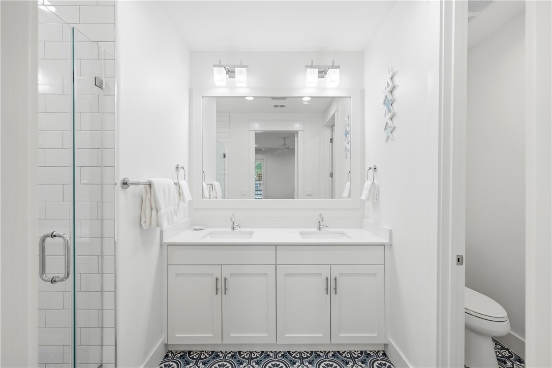 Bathroom with a double-sink vanity, glass shower, and blue-and-white patterned floor tiles.
