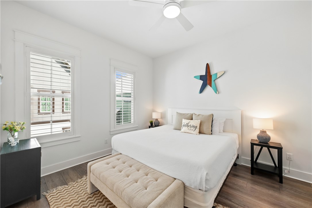Bright bedroom with a white bed, tufted bench, shuttered windows, and colorful starfish wall decoration.